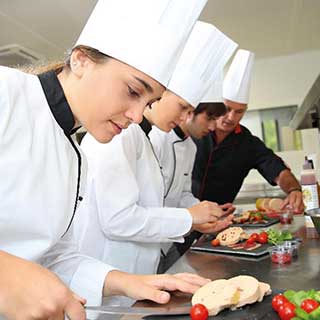 Drei junge Menschen in Kochkleidung und ein Ausbilder bereiten das Essen vor