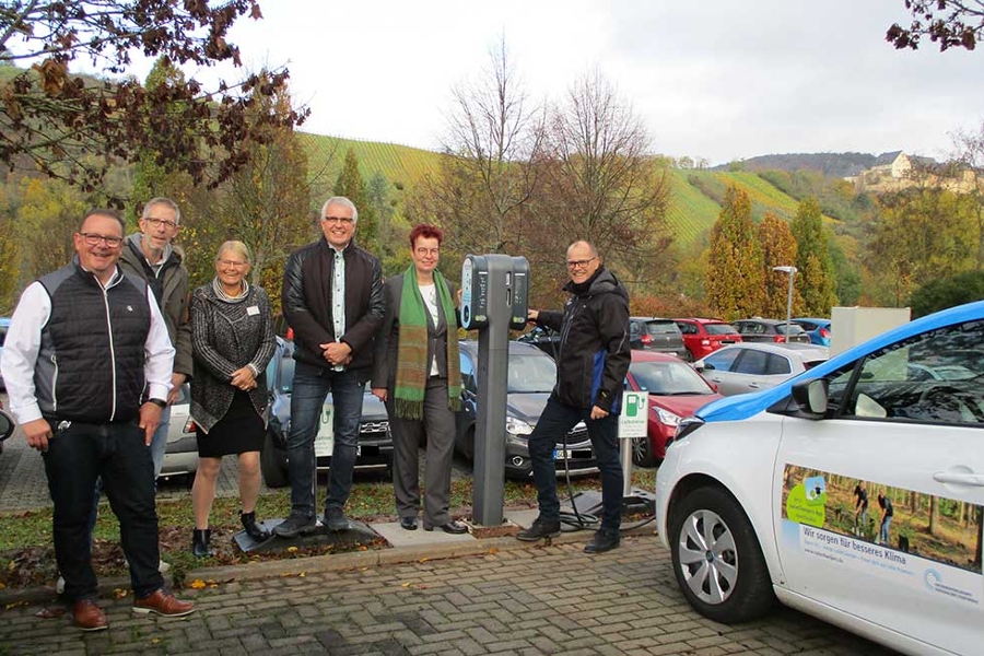 Zwei Frauen und vier Männer neben der neuen E-Ladesäule und einem Elektroauto