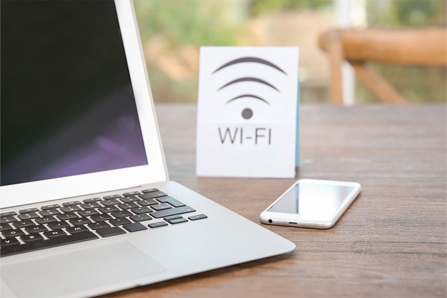 Ein Laptop und ein Smartphone liegen auf einem Tisch. Dazwischen steht ein Schild, auf dem "WIFI" steht.
