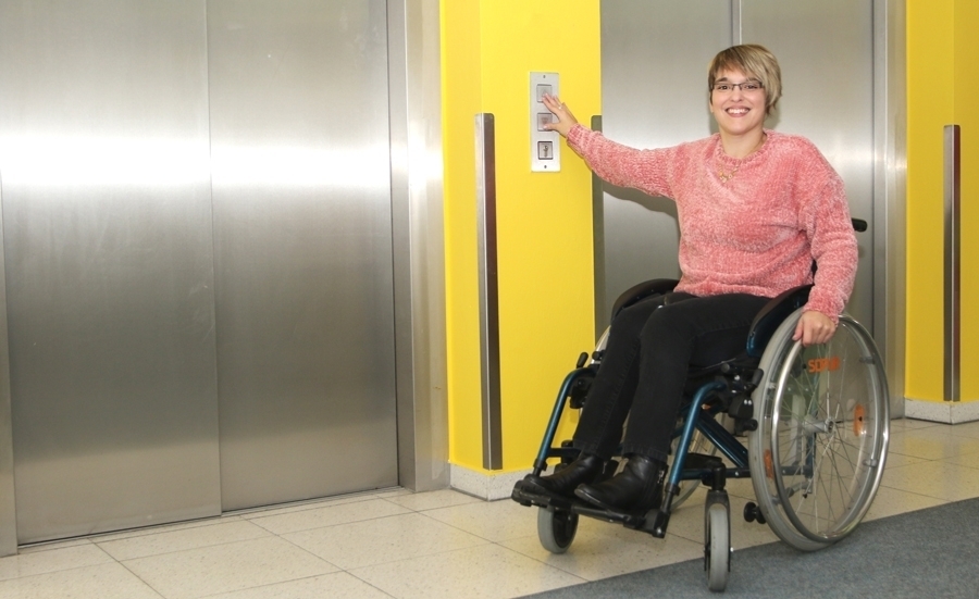 Junge Frau im Rollstuhl vor Aufzug