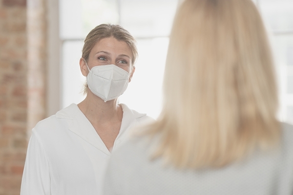 Frau mit Maske spricht mit blonder Frau im Vordergrung Frau mit Maske spricht mit blonder Frau im Vordergrung