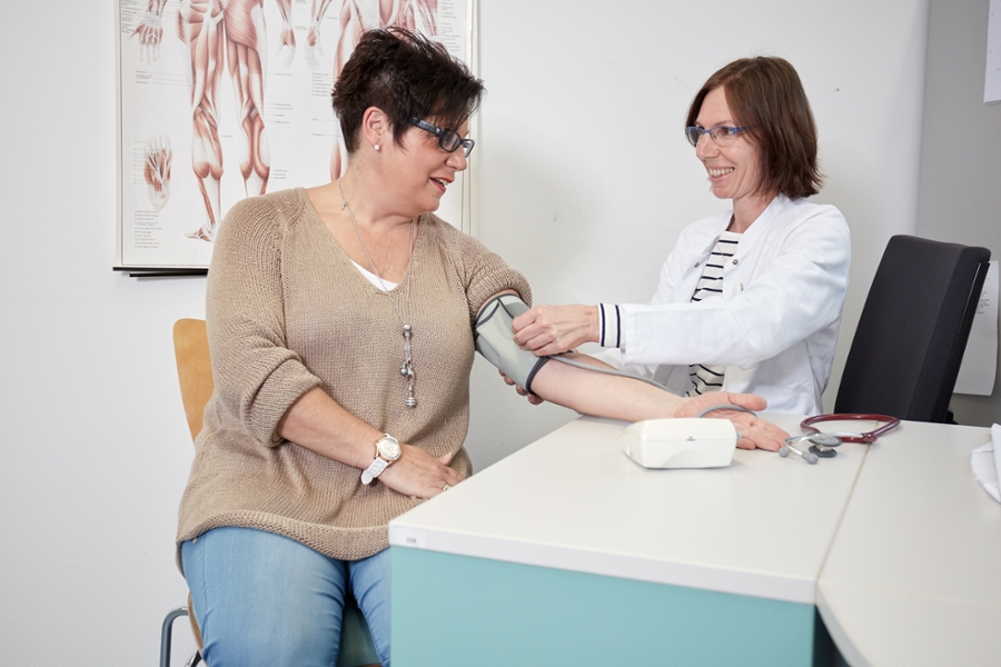 Eine Mitarbeiterin untersucht den Blutdruck einer Patienten